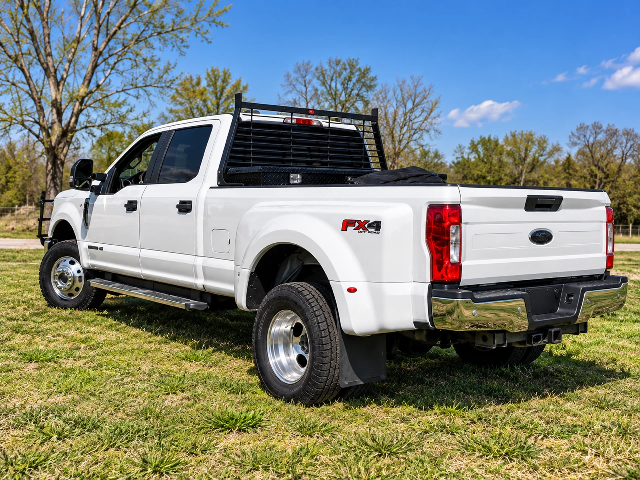 Rear three-quarter view of a white Ford F-350 dually with headache rack and toolbox